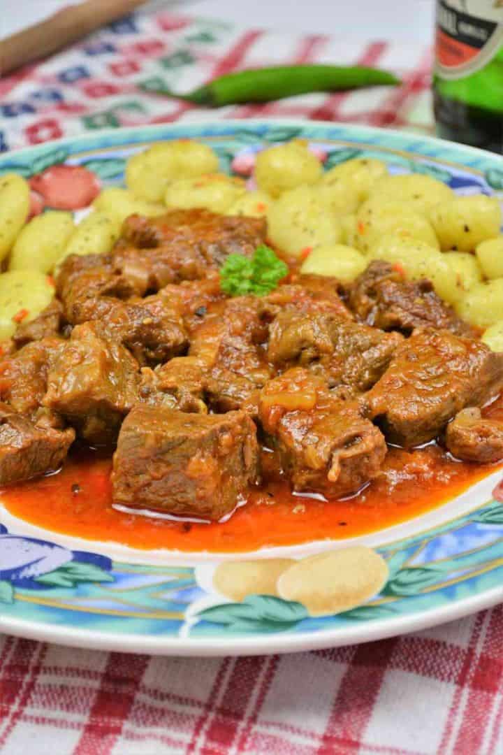 A plate of rich Hungarian Dutch oven beef stew with paprika, served over pillow-soft potato gnocchi with a fresh hot chili pepper.