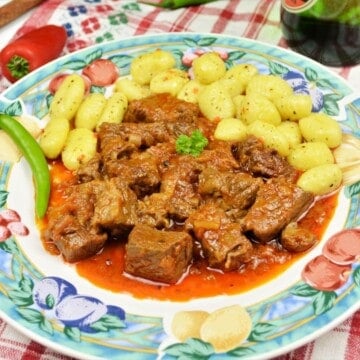 A colorful plate of rich Hungarian Dutch oven beef stew with paprika, served over pillow-soft potato gnocchi with a fresh hot chili pepper.