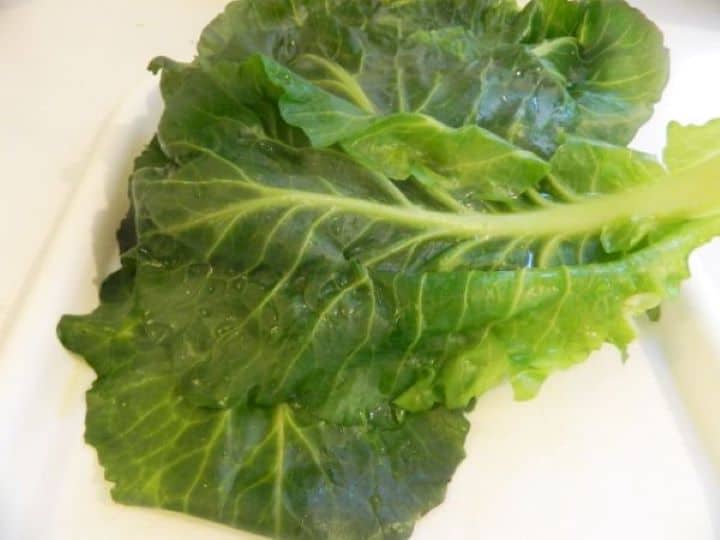 Pliable, blanched collard green leaves spread out on a white plate to cool.