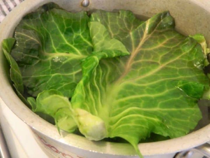 Fresh collard green leaves being blanched in a large pot of boiling salted water.