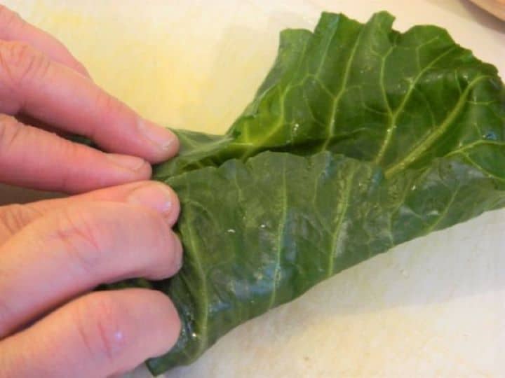 Tightly rolling a stuffed collard green from the base to the tip like a burrito.