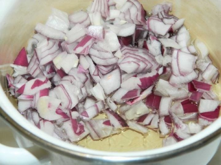 Finely chopped red and white onions frying in sunflower oil in a stainless steel saucepan.