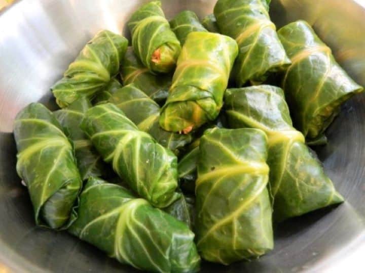 A batch of neatly wrapped, uncooked stuffed collard greens (Töltike) resting in a bowl.