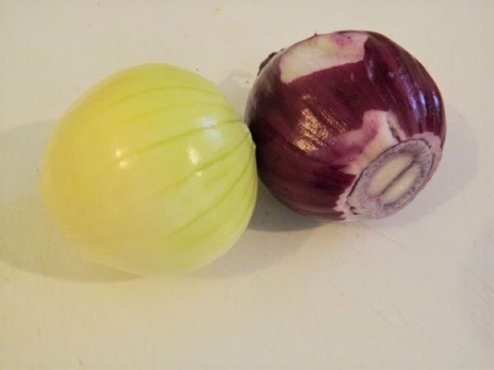 A fresh whole red onion and a white onion placed on a wooden chopping board.