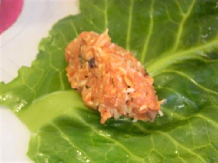 A heaping tablespoon of seasoned meat filling placed at the base of a trimmed collard green leaf.