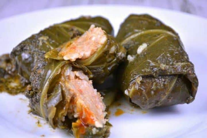 Three hot, savory stuffed collard greens served beautifully on a white plate with fresh dill and sour cream.