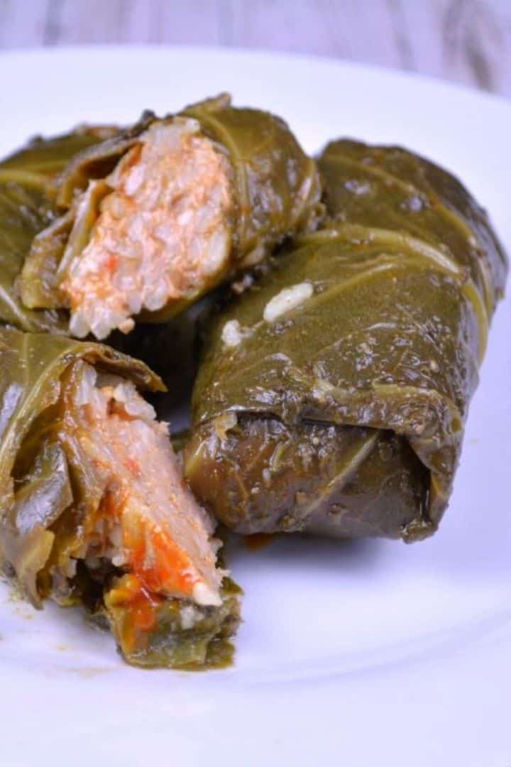 A white plate featuring a finished authentic stuffed collard greens recipe (Transylvanian Töltike) served with sour cream.