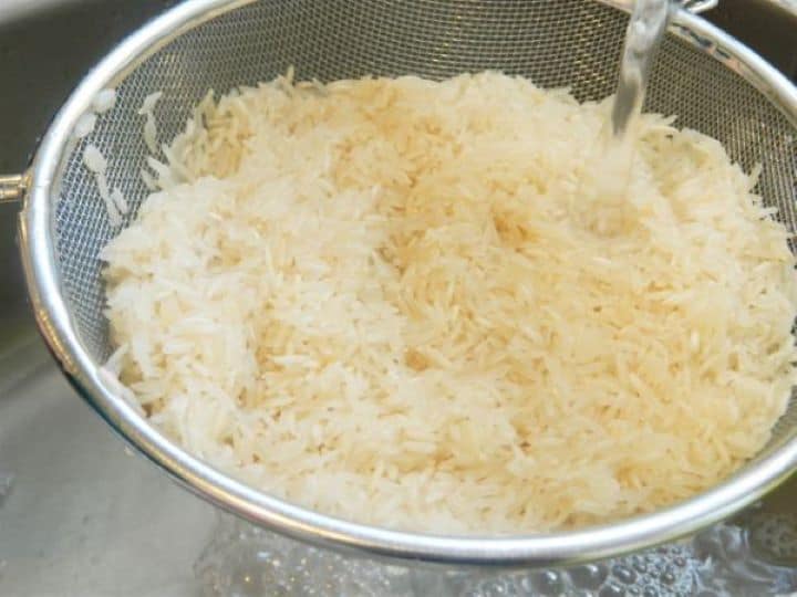 White rice being thoroughly rinsed under cold running water in a fine-mesh sieve strainer.