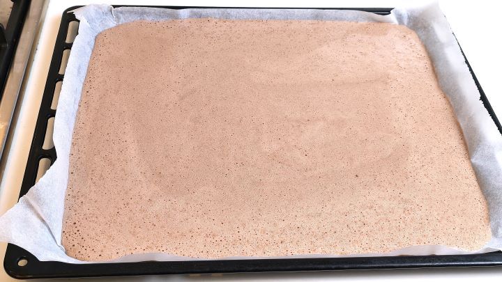 Chocolate sponge cake batter spread evenly onto a parchment-lined baking sheet.