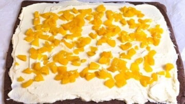 Scattering finely diced sweet peaches evenly over a mascarpone cream layer.