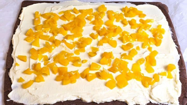 Scattering finely diced sweet peaches evenly over a mascarpone cream layer.