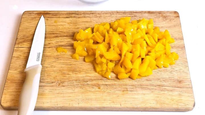 Finely diced canned peaches thoroughly drained on a cutting board.