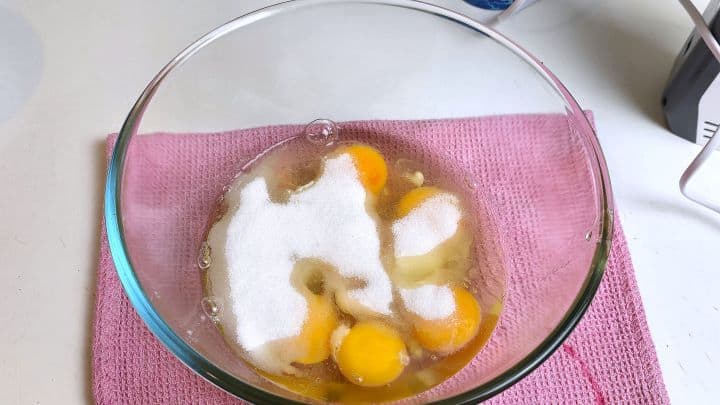 Whisking large eggs and granulated sugar in a glass bowl for a sponge cake roll.