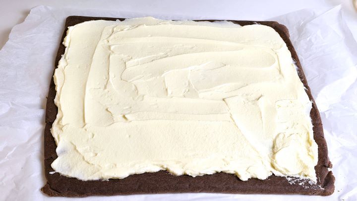 Spreading a smooth layer of velvety mascarpone cream onto an unrolled chocolate sponge.