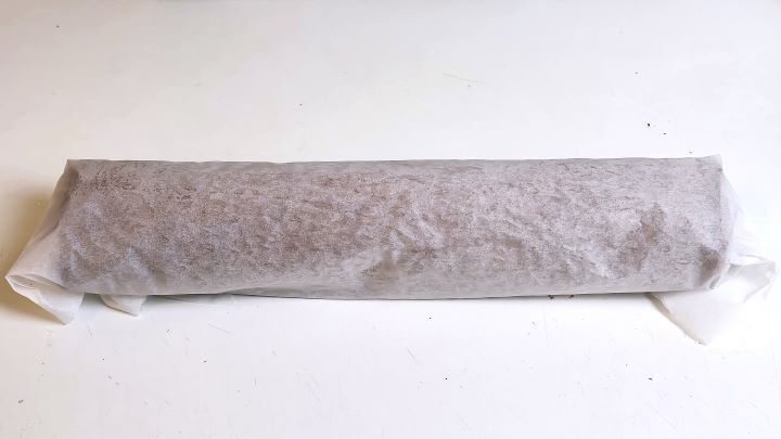 Warm chocolate sponge cake rolled into a loose cylinder with parchment paper to prevent cracking.