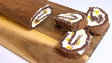 Slicing a chilled chocolate peach Swiss roll with a sharp knife to show the internal cream spiral.