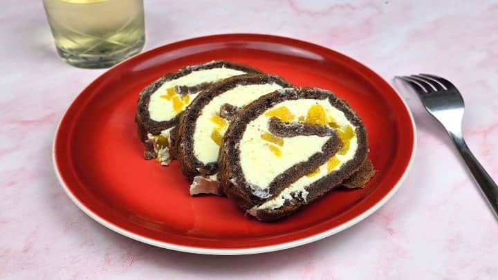 Individual servings of chocolate peach Swiss roll slices on a red plate next to a glass of refreshing fruit juice.