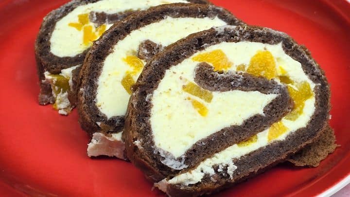 A close-up view of a single chocolate peach Swiss roll slice highlighting the airy cocoa sponge and velvety cream filling.