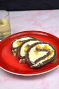 Elegant presentation of three peach mascarpone cake roll slices arranged on a festive red plate for a dinner party dessert.