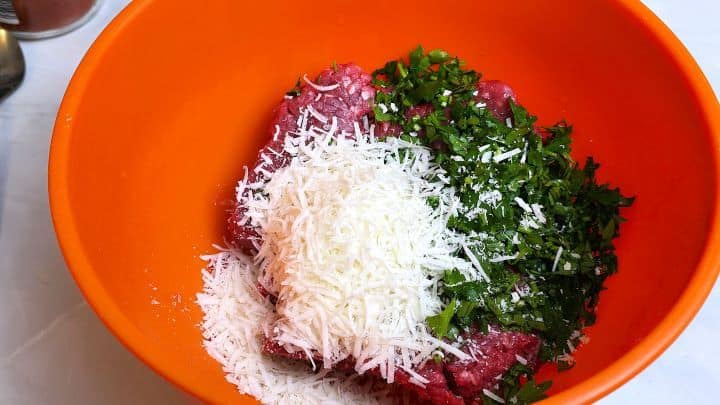 Seasoned minced beef with breadcrumbs, egg, spices, and grated Pecorino Romano cheese in a bowl.