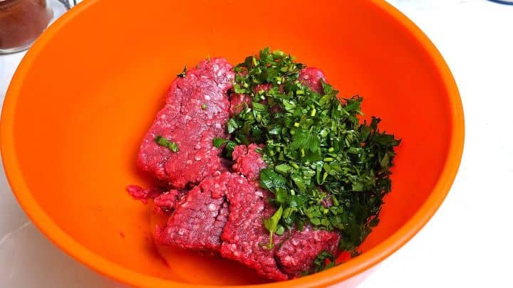 Fresh ground beef mince combined with finely chopped flat-leaf parsley in a orange mixing bowl.