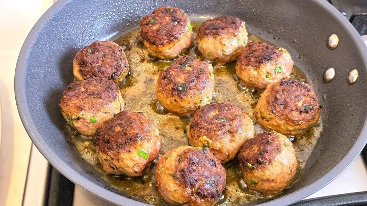 Turning the meatballs over in the skillet to fry on the other side until a golden-brown crust forms.