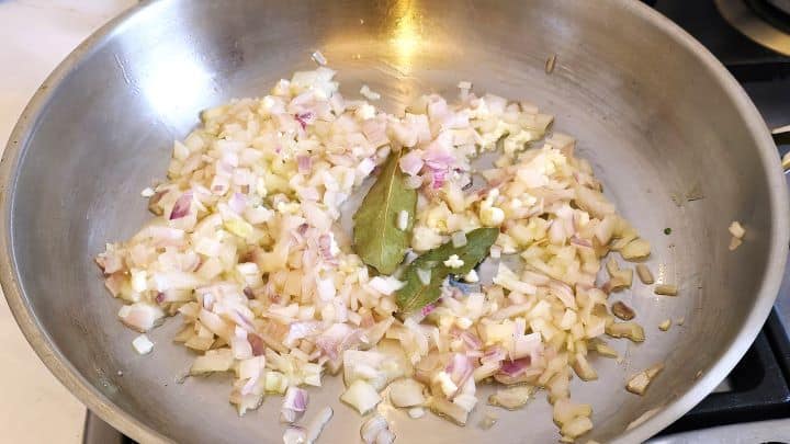 Sautéing chopped red onion, crushed fresh garlic, and dried bay leaves in a large saucepan.