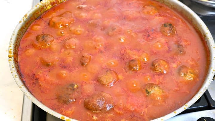 A hot pan of freshly finished Romanian meatballs in tomato sauce (chiftele marinate) ready to be plated.