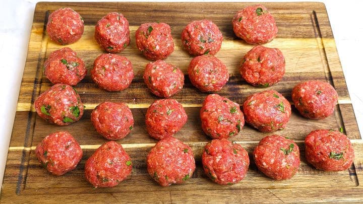 Raw beef meatballs rolled into uniform golf-ball sizes arranged on a wooden chopping board.