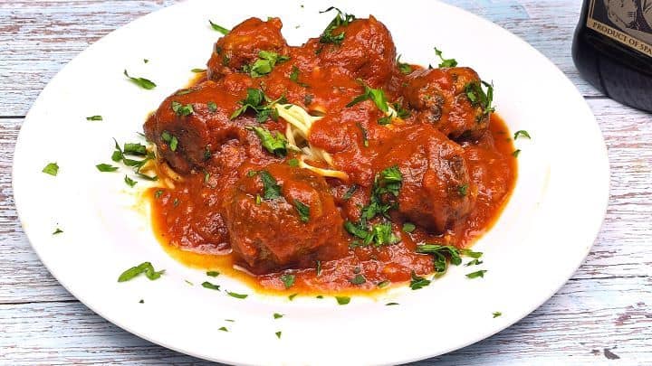 A serving of pan-seared beef meatballs covered in thick tomato passata sauce next to cooked spaghetti.
