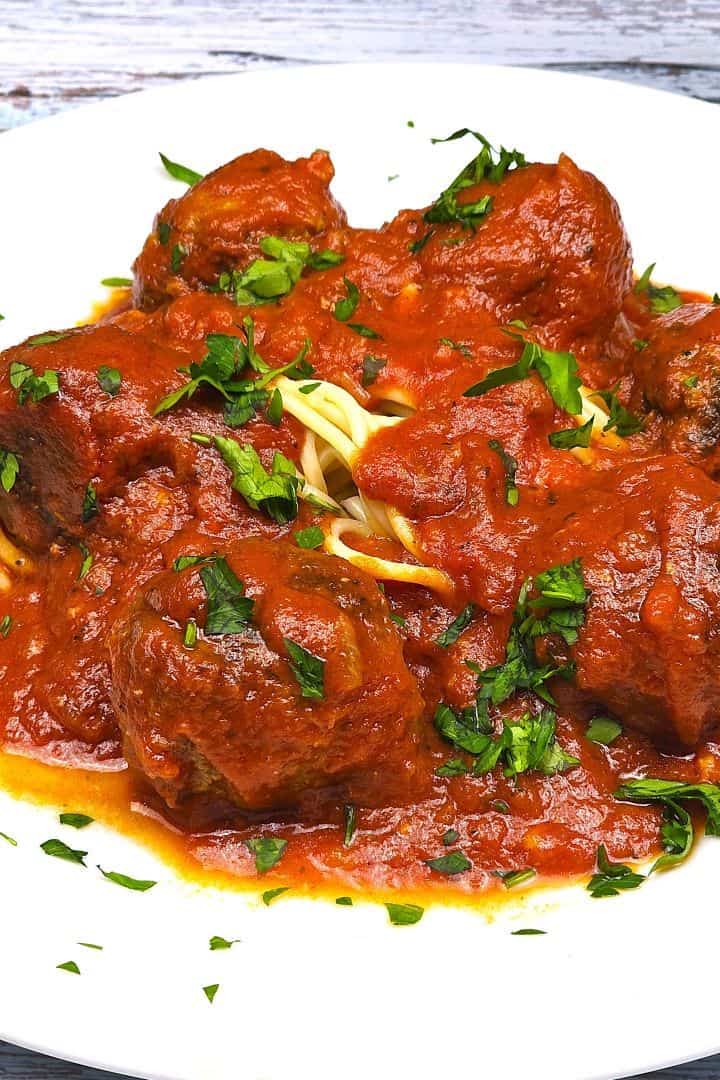 Traditional Romanian meatballs in tomato sauce (Chiftele Marinate) served on a white plate.