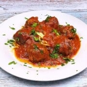 Traditional Romanian meatballs in tomato sauce (Chiftele Marinate) served on a white plate with spaghetti pasta.