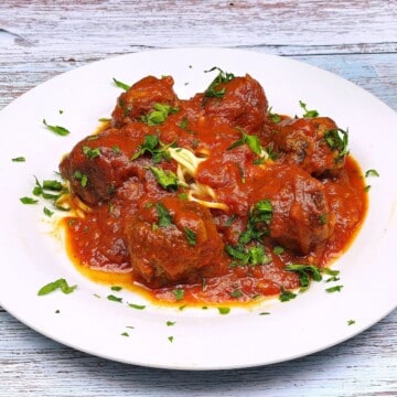 Traditional Romanian meatballs in tomato sauce (Chiftele Marinate) served on a white plate with spaghetti pasta.