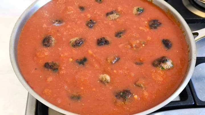 Pan-seared Romanian meatballs fully submerged and simmering gently in a rich garlic tomato passata sauce.