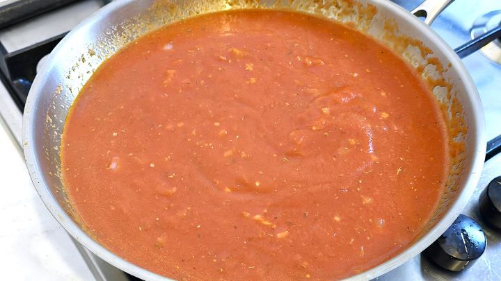 Simmering smooth tomato passata sauce with Mediterranean herbs and spices in a pan.