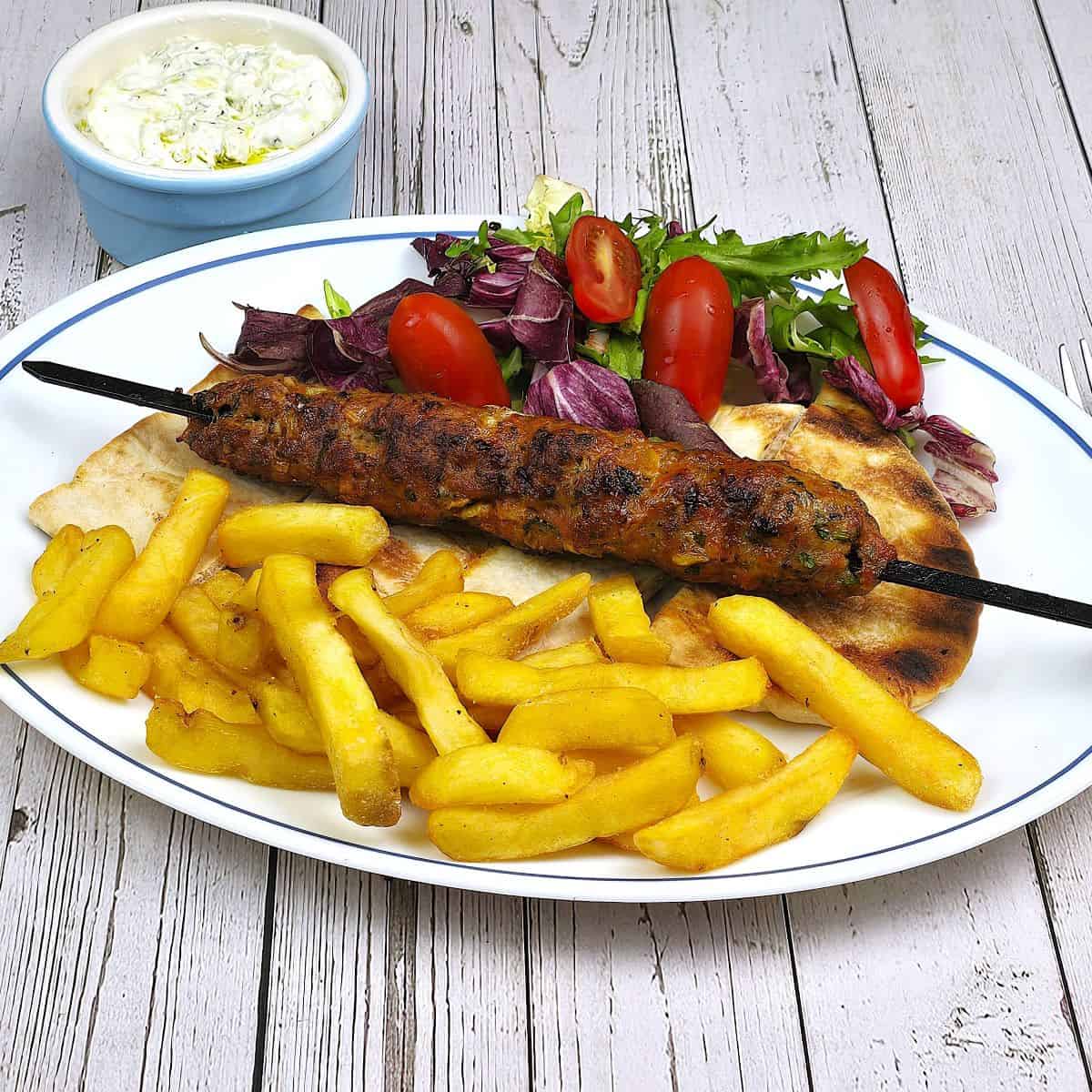 Grilled Pork Kofta Kebabs Served on White Plate With Pita, Fries and Summer Salad