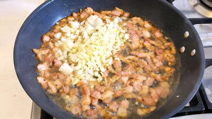 Chopped Onion and Garlic Over the Frying Bacon in the Pan