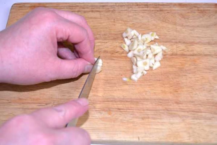 Chopping Finely chopped fresh garlic cloves on a wooden cutting board for duck seasoning paste.