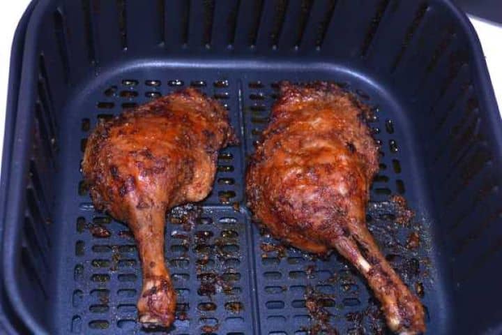 Ready Crispy golden brown air fryer duck legs resting in basket before serving.