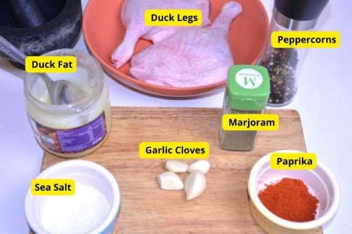 Ingredients Raw duck legs surrounded by garlic cloves, dried marjoram, sweet paprika, and duck fat for seasoning.