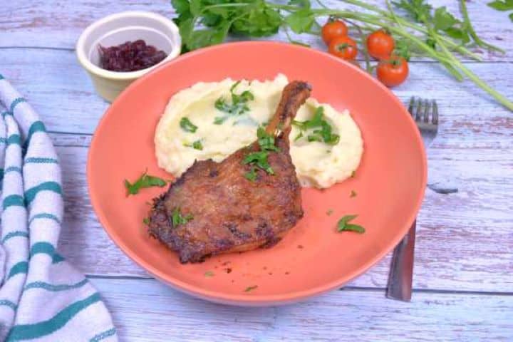 Crispy air fryer duck leg served on a plate with creamy mashed potatoes and fresh herbs.