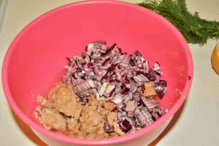 Chopped Onion and Tuna Finely diced red onion added to tuna chunks in a mixing bowl for crunchy texture and sharp flavor.