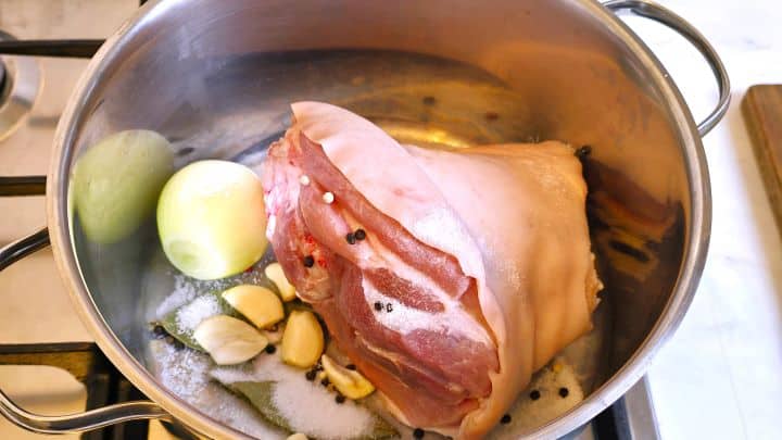 Knuckle and Onion Seasoned With Salt, Peppercorns, Garlic Cloves and Bay Leaves in the Soup Pot