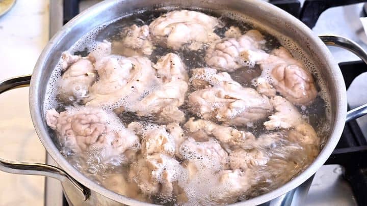 Cleaned pork brains simmering in a boiling pot of water with a bay leaf and black pepper for a traditional Transylvanian recipe.