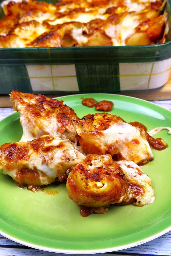 Four cheesy chicken stuffed shells served on a green plate with rich tomato sauce.