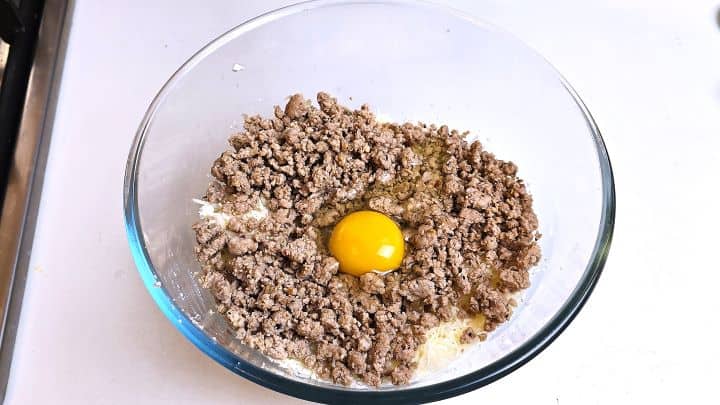 Bowl containing cooled chicken mince mixed with egg, crumbled feta, mozzarella cheese, and Italian herbs.