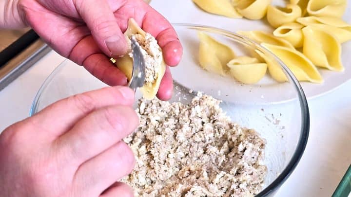 Spooning cheesy chicken filling into a jumbo pasta shell.