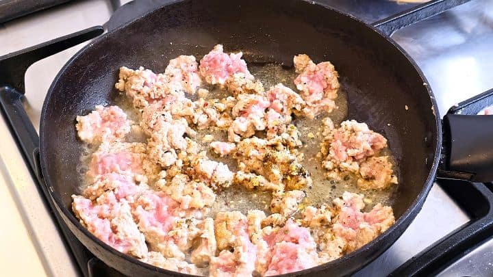 Sautéing seasoned ground chicken mince in a skillet with olive oil, black pepper, and Italian spices.