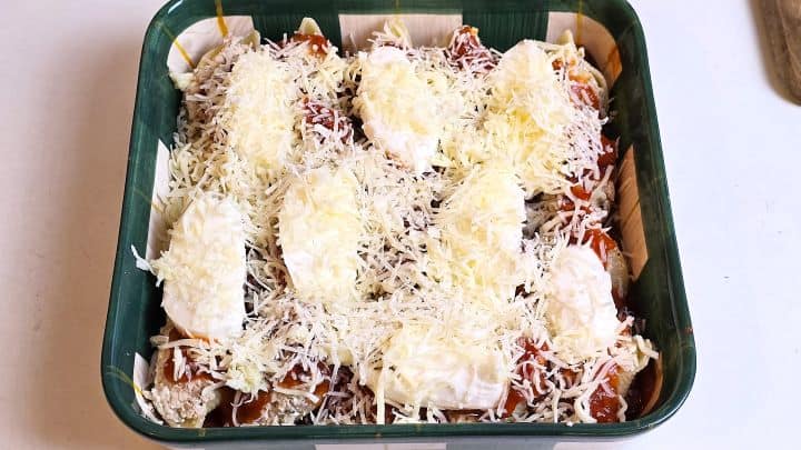 Stuffed pasta shells topped with sliced mozzarella balls, tomato sauce, grated mozzarella, and Pecorino Romano before baking.