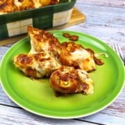 Four cheesy chicken stuffed shells served on a green plate with rich tomato sauce.